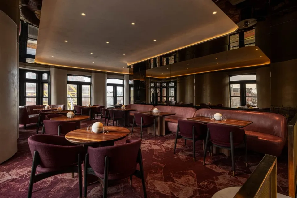 An elegant restaurant dining room with plum banquettes and warm lighting